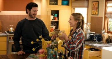 "A man and woman smile and toast with mugs in a cozy, sunlit kitchen, surrounded by yellow cabinets, kitchen appliances, and decorative items, creating a warm, homey atmosphere."